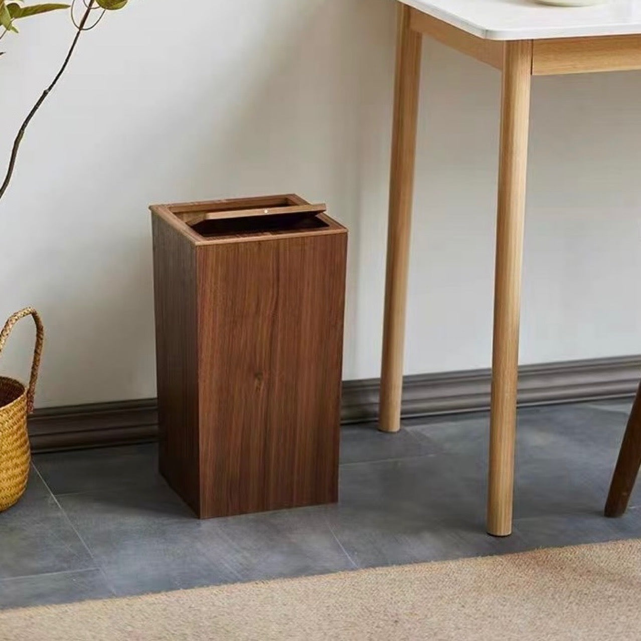 Wooden trash can next to a table on a tiled floor.