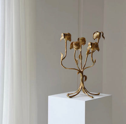 Gold floral candelabra on a white pedestal against a gray wall