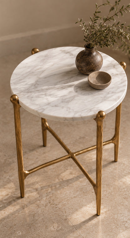 Natural white marble tabletop and sculptural antique gold metal frame. A round marble-top accent table with a gold metal frame and decorative vase and bowl on top, photographed in a warm neutral interior setting.