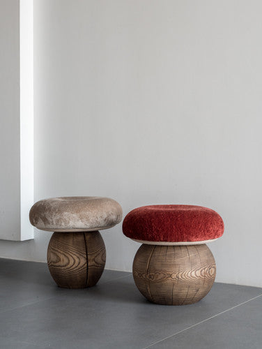 Two mushroom-shaped wooden stools in a minimalist room. The left stool has a textured beige velvet cushion on a dark brown wood base.