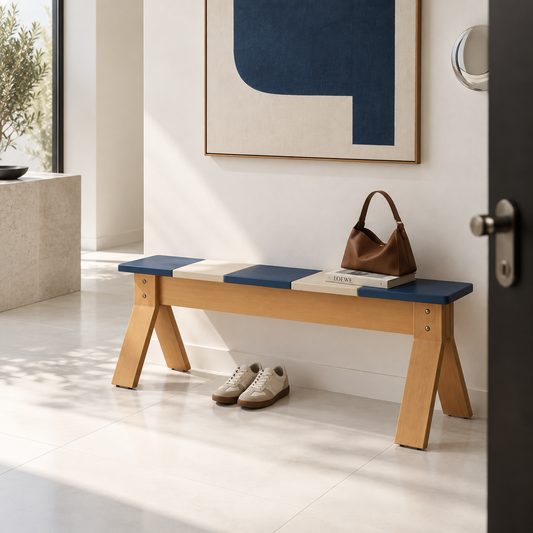 A modern wooden entryway bench with a blue and cream upholstered seat, styled in a bright minimalist hallway with a brown handbag, books, and a pair of beige sneakers underneath.