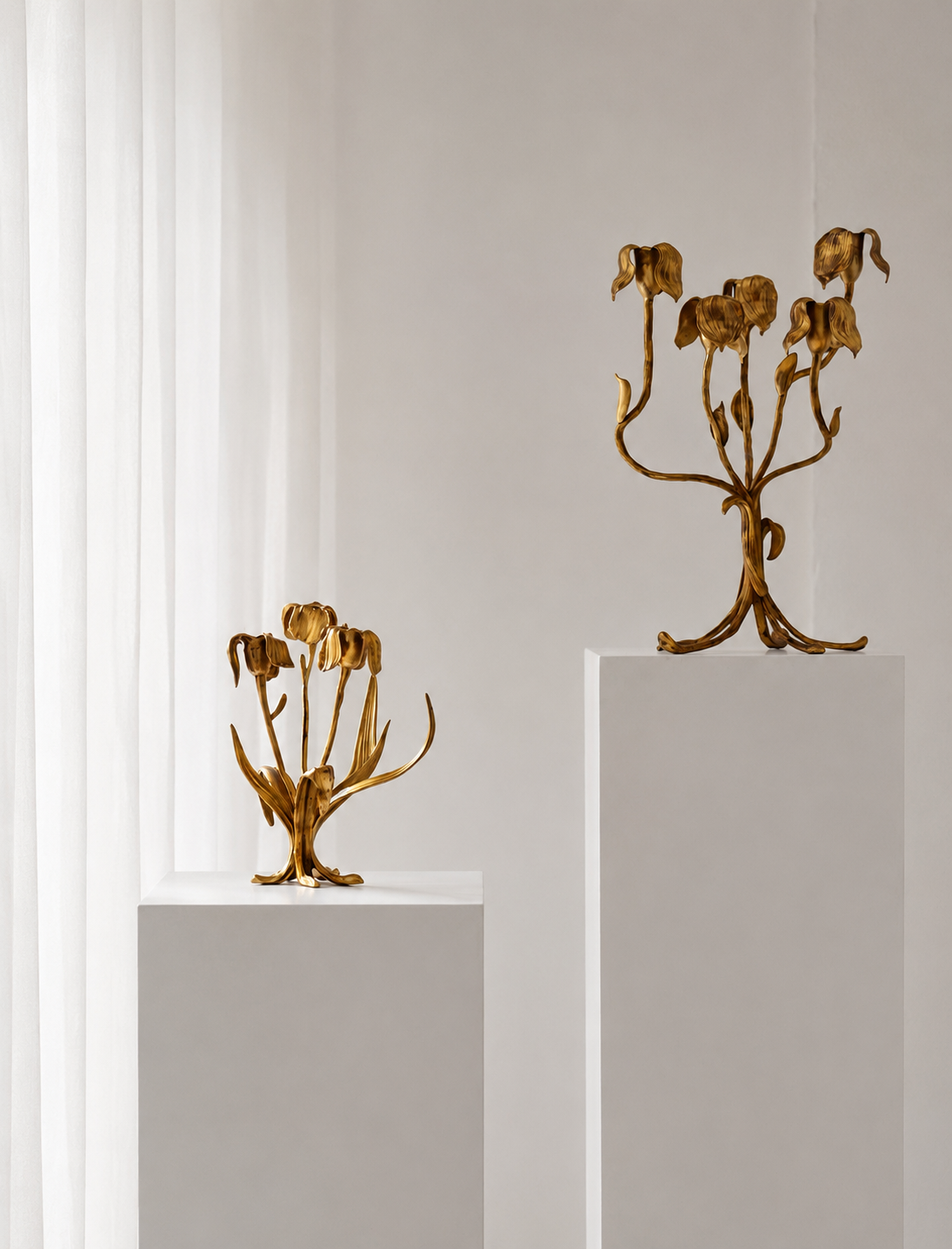 Two gold candelabras on white pedestals against a light gray wall.