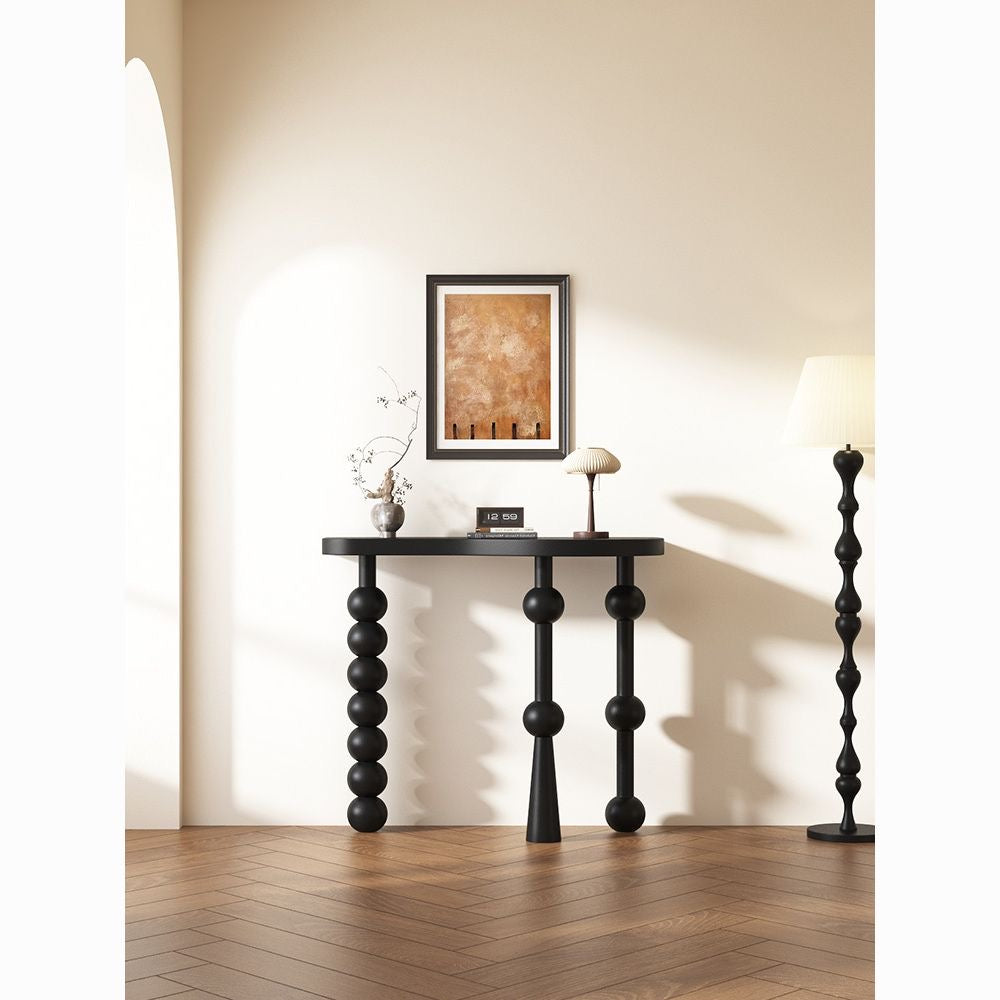 Matte black sculptural console table with spherical legs in a modern minimalist hallway.