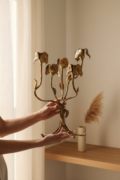 Gold floral candle holder held by a person against a neutral background