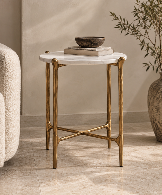 Ausi sculptural white marble side table with antique gold metal legs. A small round side table with a white marble top and textured gold metal legs, styled in a warm, modern living room setting.