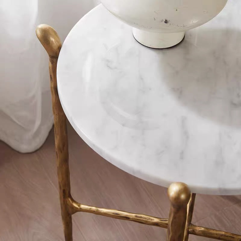 Ausi round marble table with gold legs and a white lamp on a wooden floor.
