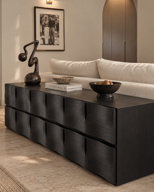 Ausi modern black wooden coffee table with a textured, wavy ribbed drawer front, styled in a warm, contemporary living room next to a cream sofa.