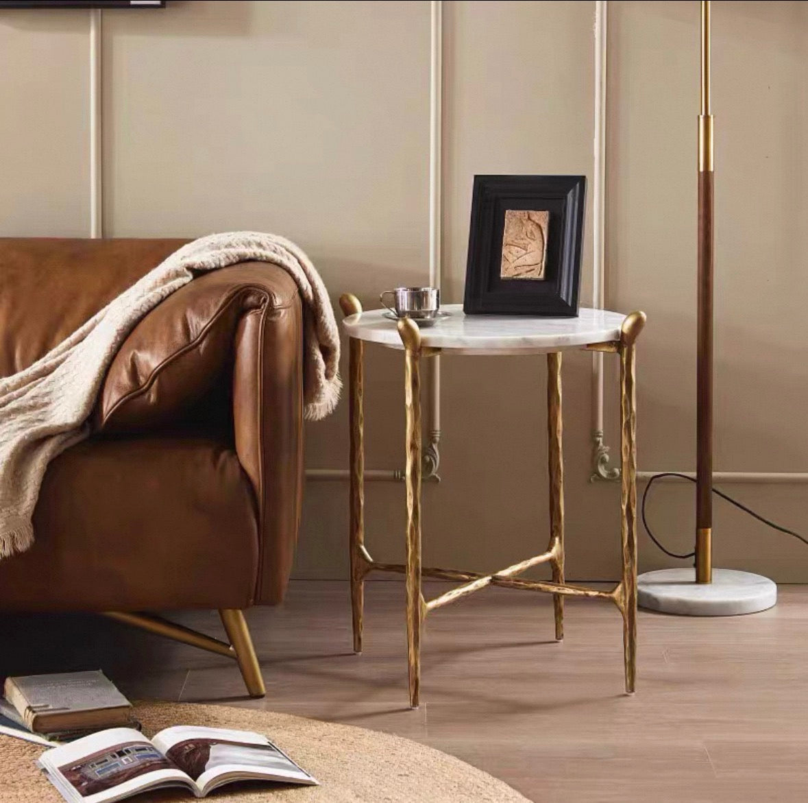 Ausi marble side table with a white marble top and twisted gold metal legs, styled in a living room next to a brown leather armchair and a floor lamp.