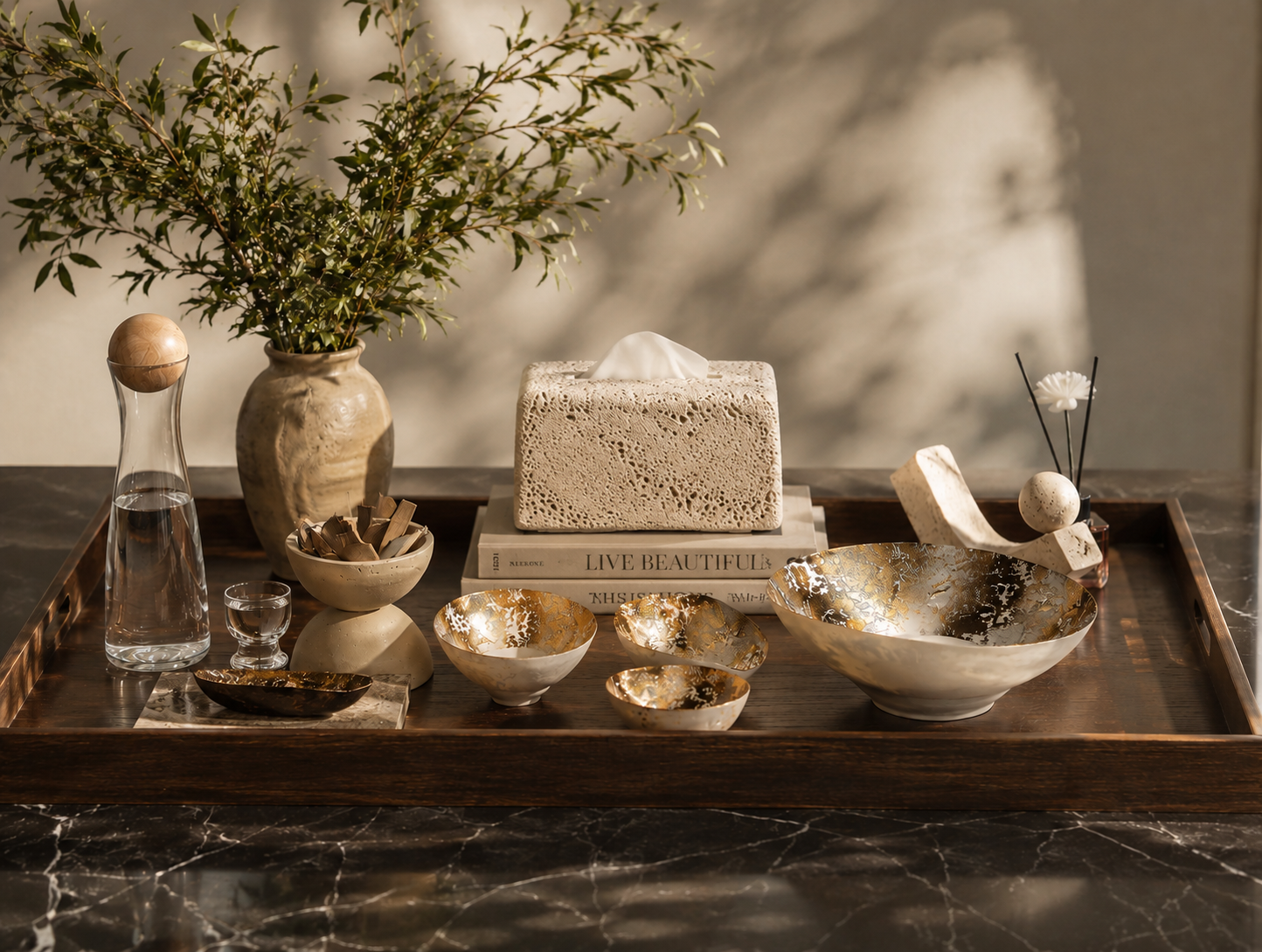 Decorative tray with various items including a vase, bowls, and a book on a marble surface.