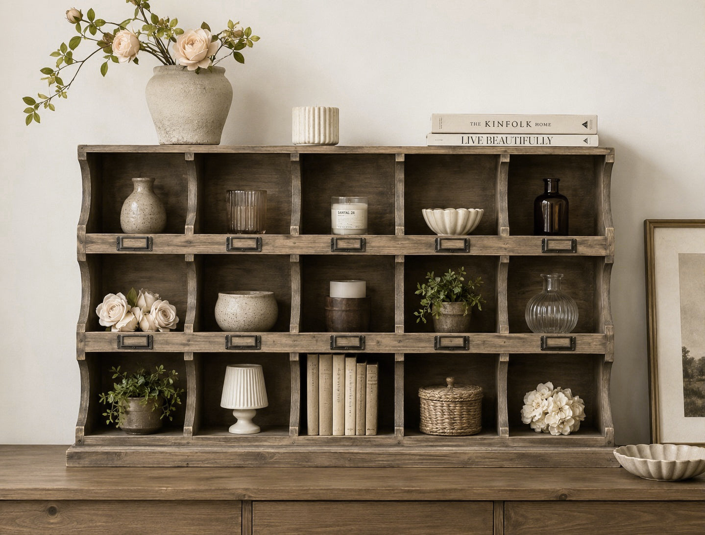 A rustic wooden 3x5 open shelving cabinet with 15 individual cubbies, styled with home decor items including vases, books, candles, and small plants, set against a neutral wall.