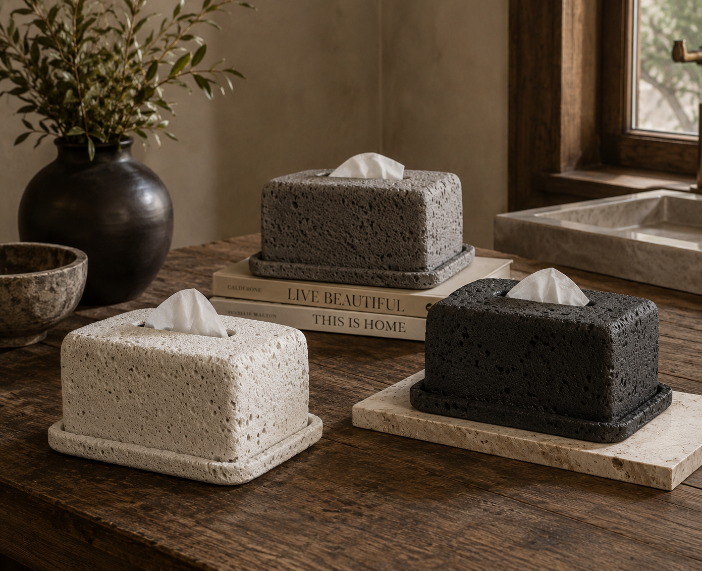Three square tissue holders made of textured material on a wooden surface with a vase and books in the background.