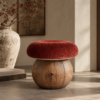A round wooden stool with a thick, cushioned red velvet seat in a warm, rustic interior setting.