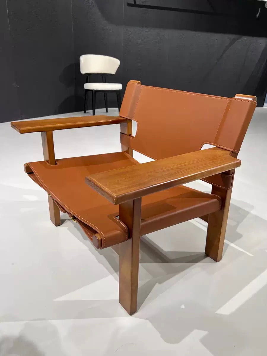 A modern wooden lounge chair with a warm brown leather seat, backrest, and armrests, shown in a showroom setting.