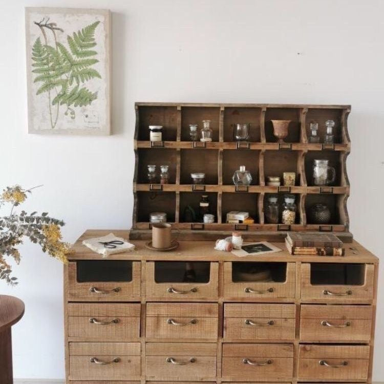 Wooden cabinet with shelves and drawers in a room with a plant and framed picture on the wall.
