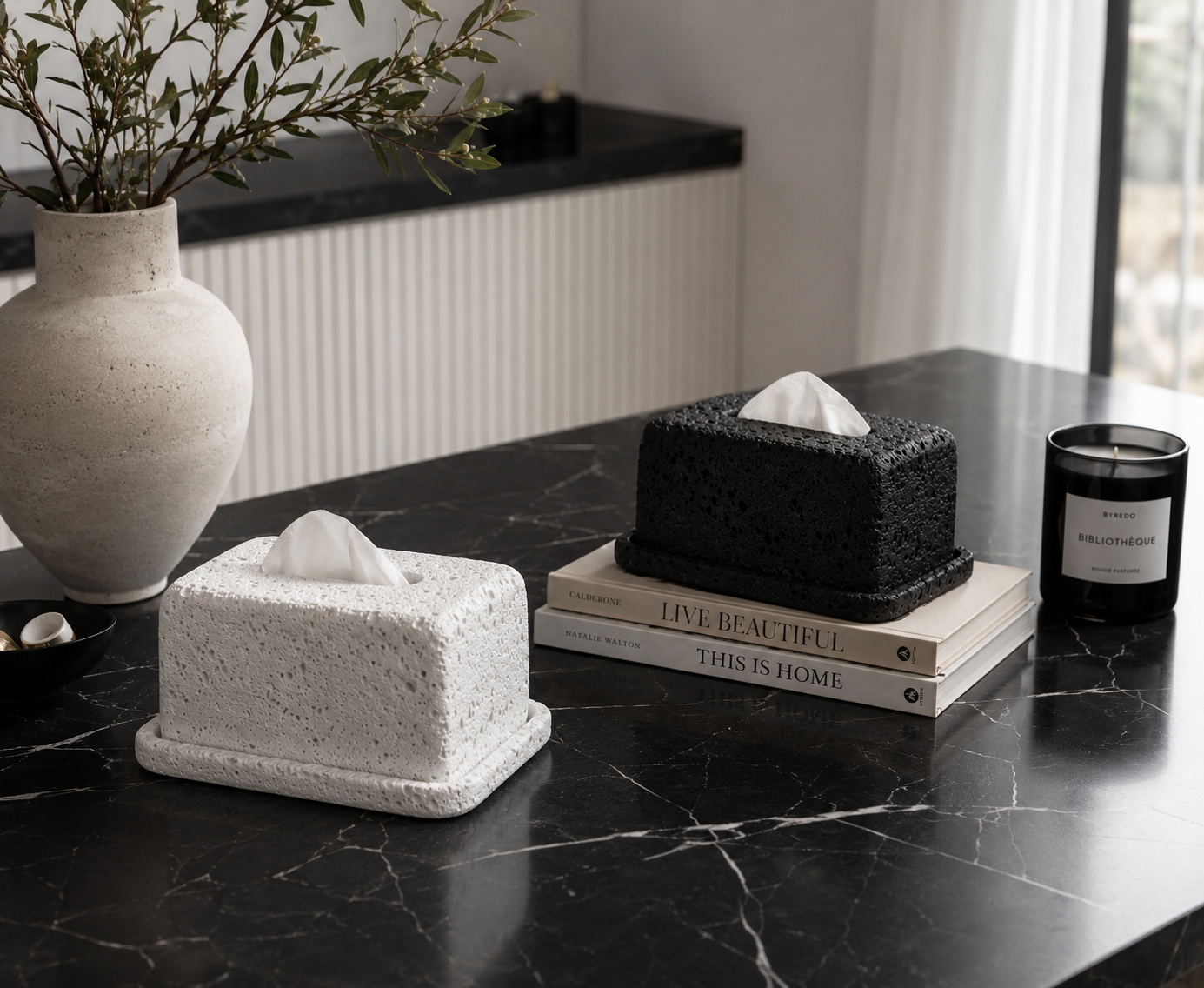 Decorative tissue boxes on a black marble surface with a candle and vase in the background.