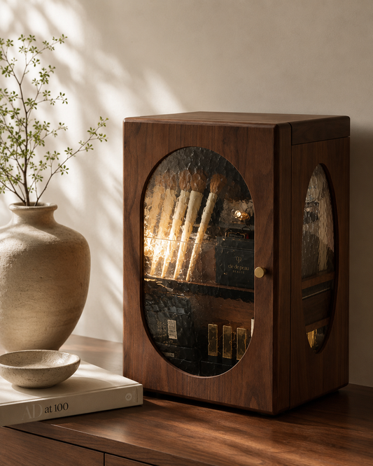 Wooden cabinet with glass door displaying items, placed on a wooden surface with a plant and books in the background.